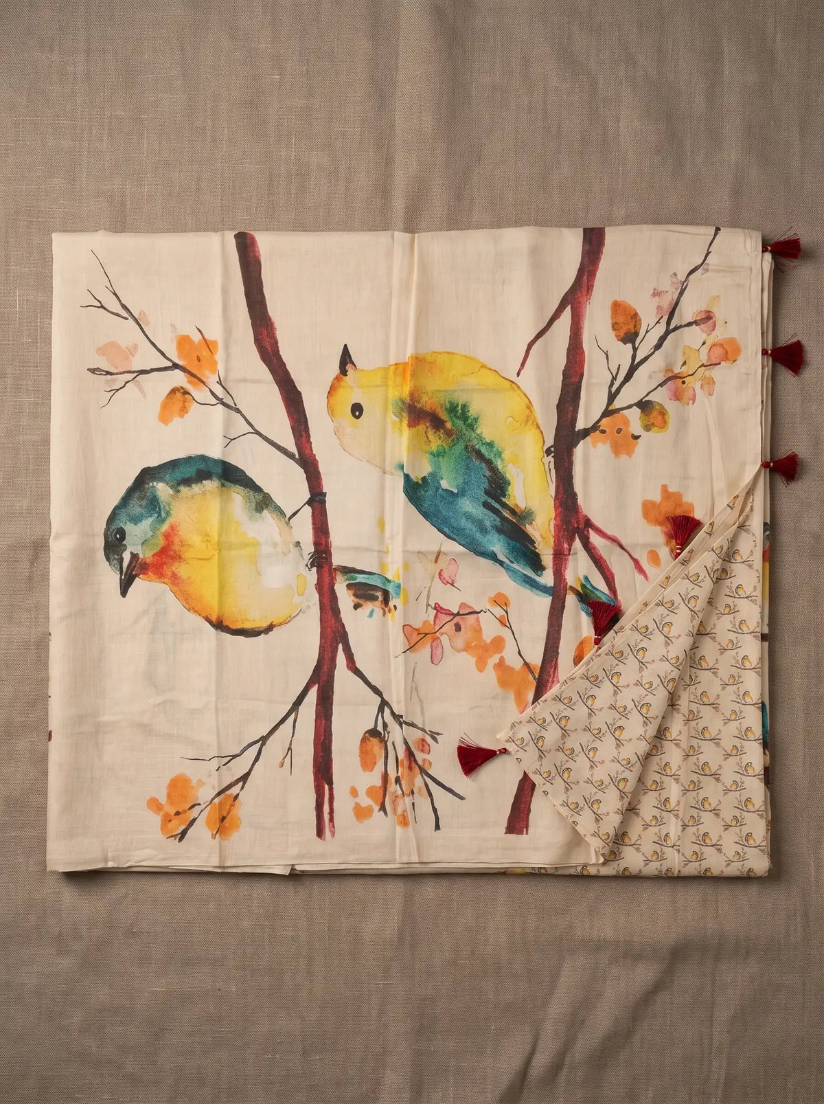Beige linen saree displayed flat with colourful bird and branch print, printed blouse piece and maroon pallu tassels