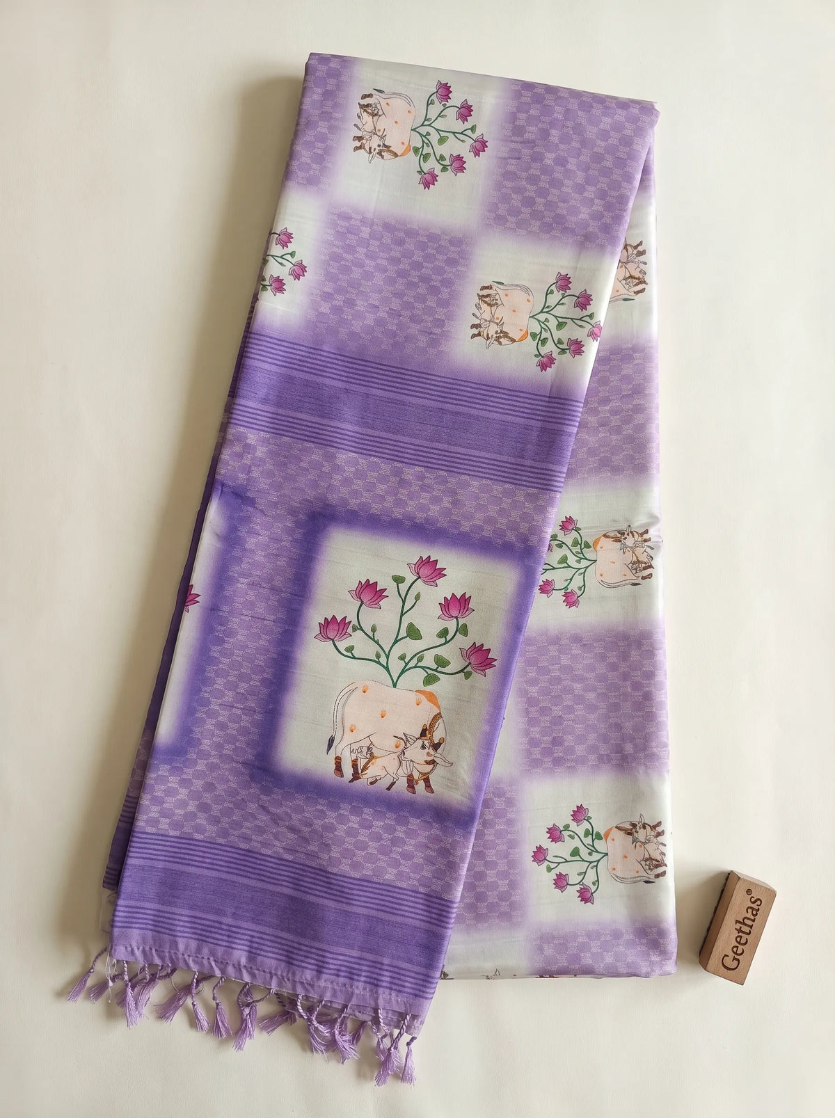 Folded white and violet printed slub linen saree showing floral and cow motifs, geometric panels, striped border and tassled pallu