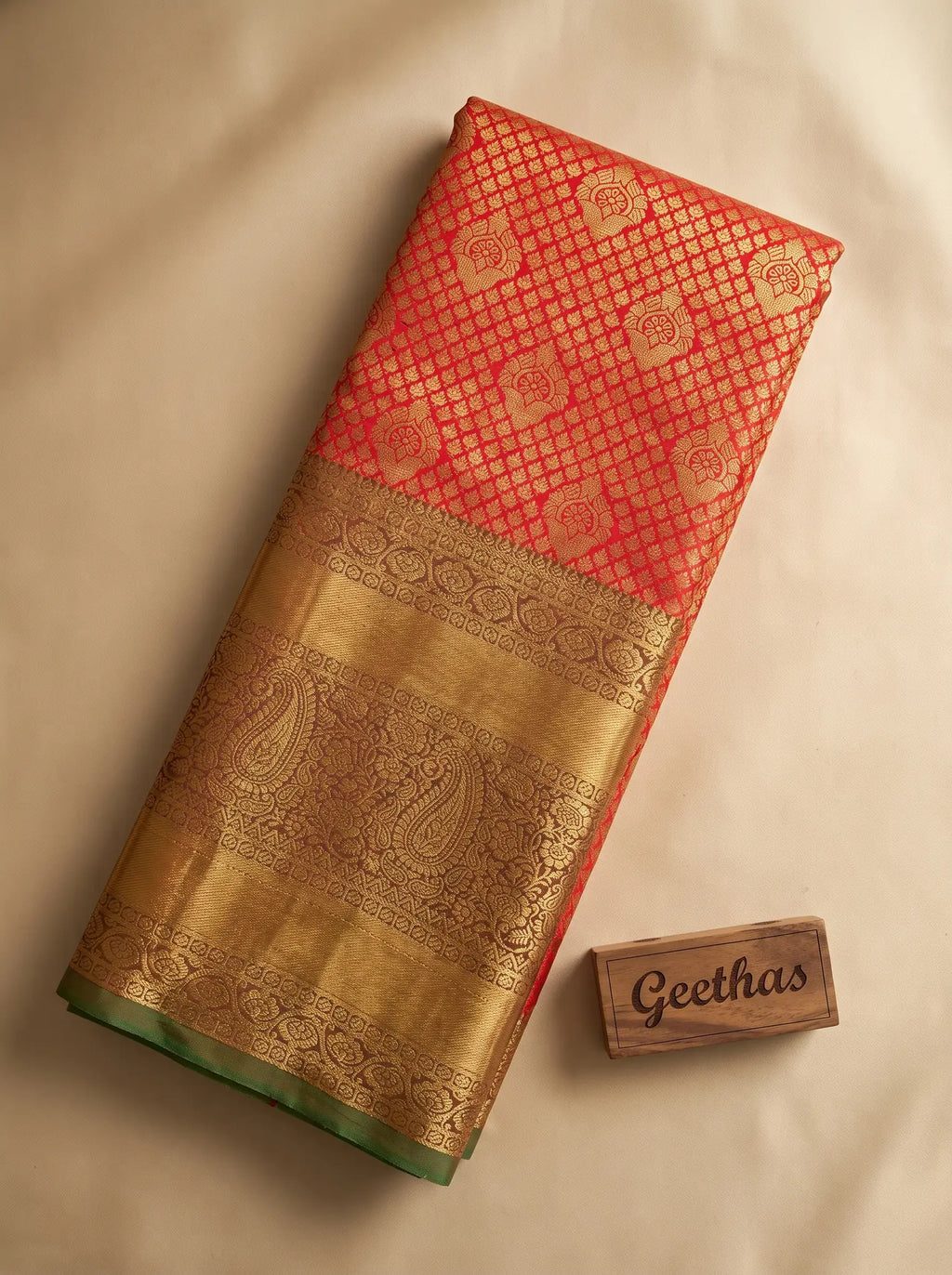 Vermilion orange semi silk saree folded to display its gold-toned woven paisley border and green edging