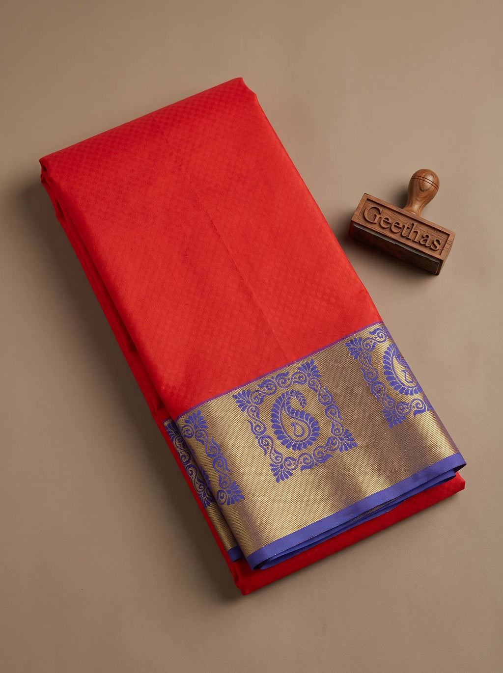 Folded orange semi silk saree showing the royal blue and antique gold paisley woven border