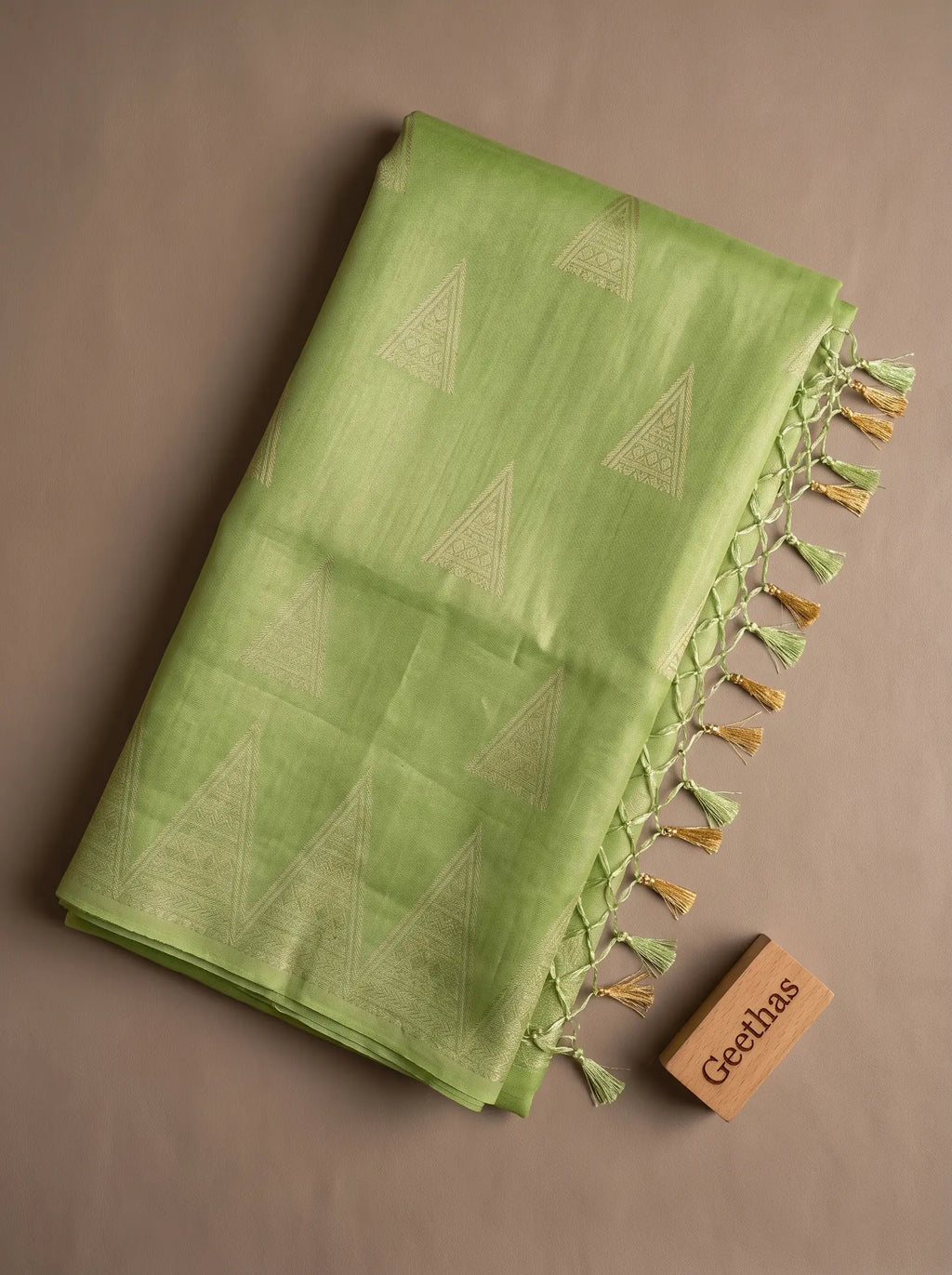 Folded pista green soft tissue saree with woven geometric motifs and green and gold-toned tassled pallu