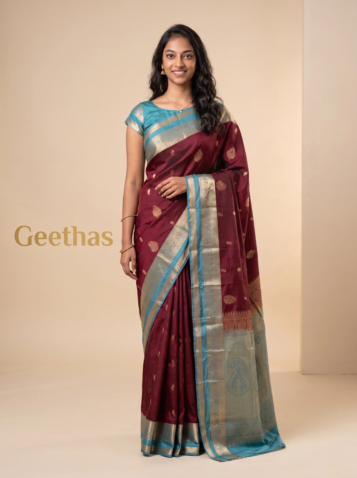 Model wearing a maroon soft silk saree with gold-toned woven motifs and a turquoise blue decorative border