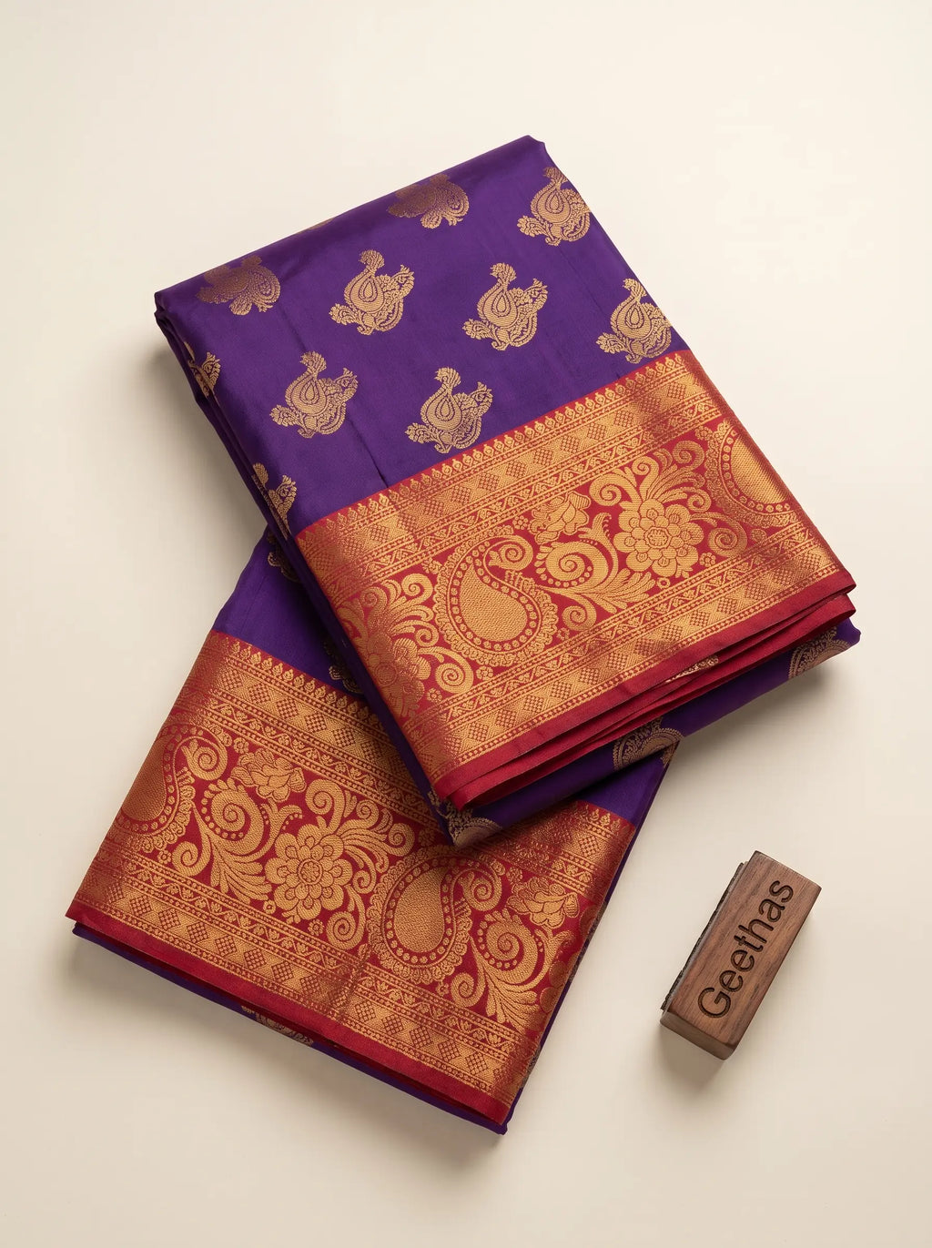 Folded violet soft silk saree with gold-toned paisley motifs and deep red woven border