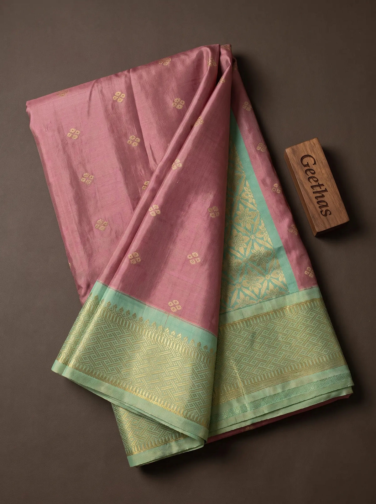 Folded onion pink soft silk saree showing gold-toned motifs and sea green woven geometric border